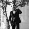 A man in a tuxedo adjusts his sunglasses outdoors, exuding elegance and style.